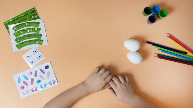 Les mains des enfants font une décoration de Pâques sur l'œuf. Crayons et autocollants sur fond jaune. Notion de Pâques. Copiez l'espace.