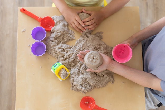 Mains d'enfants jouant avec du sable cinétique et des jouets sur la table