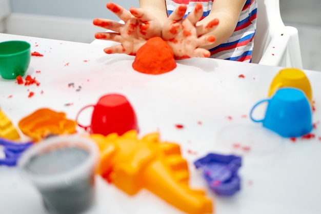 Les mains des enfants jouent avec du sable et des moules cinétiques brillants sur une table blanche