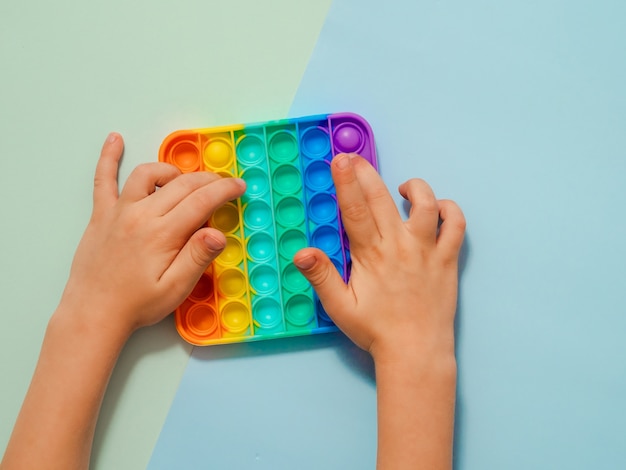 Les mains des enfants jouent avec un jouet popit sur fond bleu