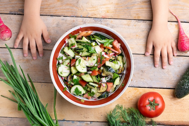 Mains d'enfants préparant une salade fraîche et saine près d'une variété de légumes et de fruits sur une table en bois, mise à plat