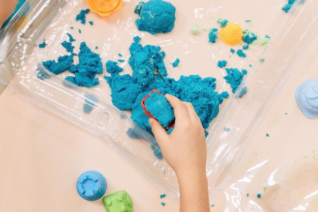 Les mains des enfants de sable cinétique jouent avec du sable polymère multicolore