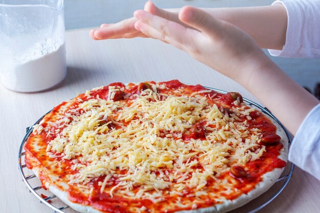 Mains d'enfants saupoudrer de fromage sur la pâte à pizza