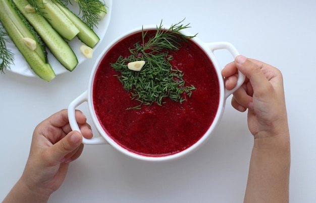 Les mains des enfants avec une tasse de soupe froide de betterave aux herbes