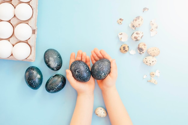 Mains d'enfants tenant des oeufs de Pâques de couleur bleue près d'oeufs blancs et de coquilles d'oeufs sur fond bleu clair Vue de dessus Concept de Pâques