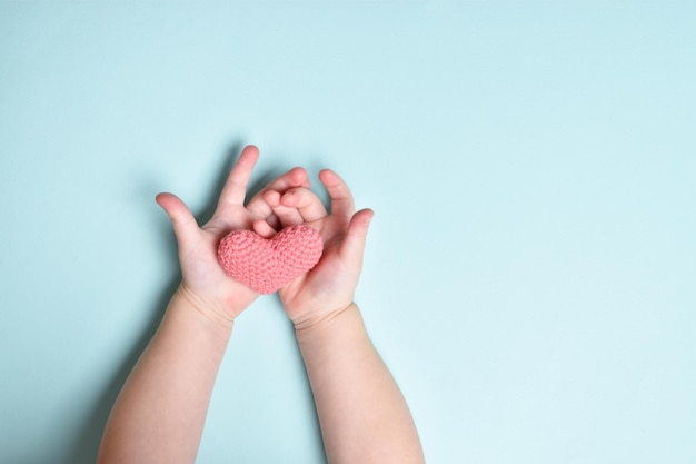 Les mains des enfants tiennent un petit coeur tricoté rose sur fond bleu. Aimer. Don d'organe. La Saint-Valentin. Journée mondiale de la santé. Fête des mères. Espace pour copier. Position à plat, vue de dessus. le jour de la saint valentin