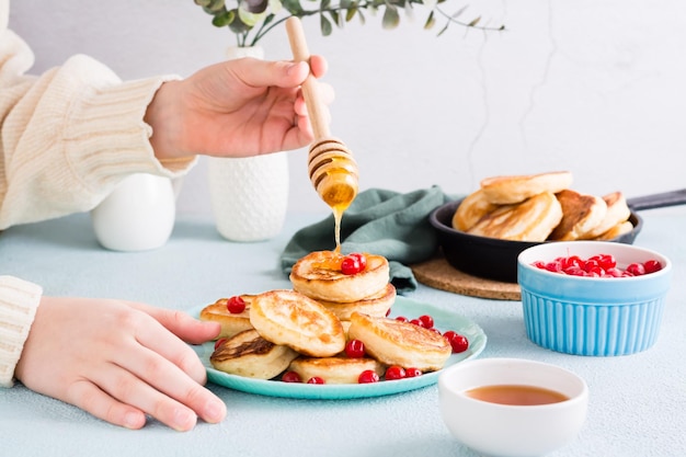 Les mains des enfants versent du miel sur des crêpes et des canneberges sur une assiette Dessert de petit-déjeuner fait maison