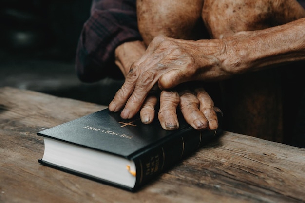 Les mains ensemble dans la prière à Dieu avec la bible Dans le concept chrétien et la religion Oldman prie dans la Bible