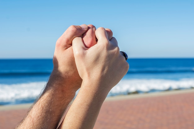 Mains entrelacées d'un couple amoureux. Avec la mer et le ciel bleu en arrière-plan.