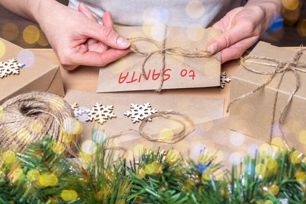 Les mains enveloppent une lettre de Noël dans une enveloppe avec les mots AU PÈRE NOL sur une table avec Christm