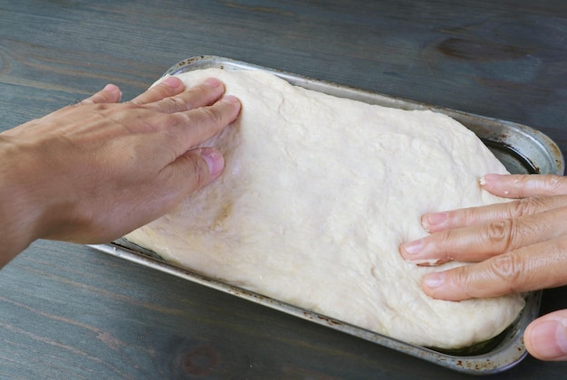 Mains étirant la pâte levée dans une casserole pour faire cuire la pizza