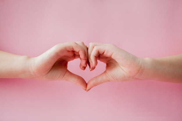 Mains faisant un coeur sur fond rose