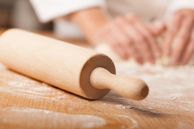 Mains faisant cuire la pâte avec un rouleau à pâtisserie sur une table en bois