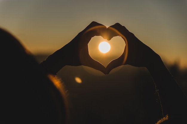 Photo mains faisant la forme d'un cœur avec le soleil au milieu