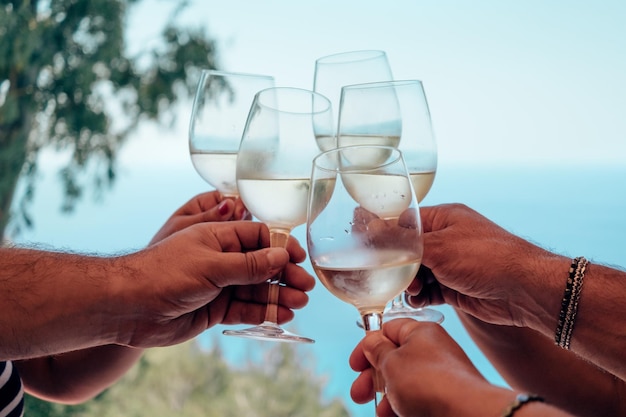 Mains faisant tinter des verres à vin au bord de la mer