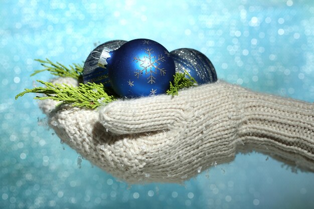 Mains femelles dans des boules d'arbre de Noël de mitaines, sur le fond de couleur