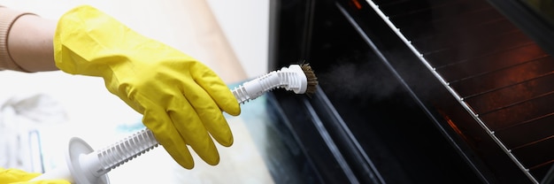 Les mains femelles dans les gants jaunes tiennent un nettoyeur à vapeur et nettoient le nettoyeur à vapeur de four pour