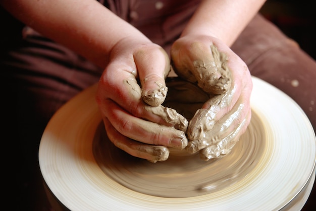 Mains femelles formant le pot d'argile sur la roue de poterie