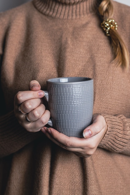 Mains femelles à la maison confortables tenant la tasse chaude de thé