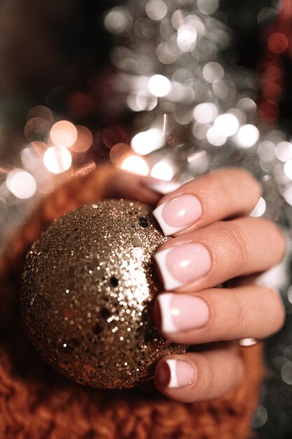 Mains femelles avec la manucure française tenant un jouet de boule de Noël d'or Lumière de bokeh de nouvelle année