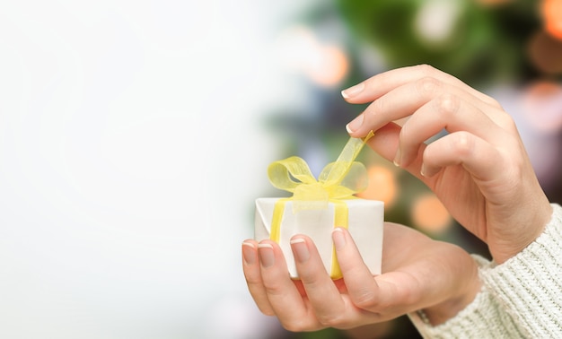 Les mains femelles ouvrent un cadeau de Noël sur le fond d'un arbre de Noël