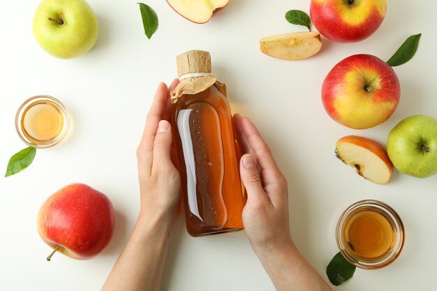 Les mains femelles tiennent le vinaigre de pomme fait maison sur le blanc