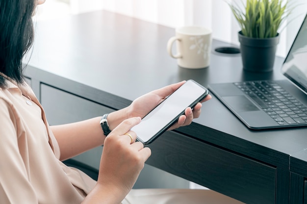 Mains féminines à l'aide de smartphone alors qu'il était assis au bureau à domicile