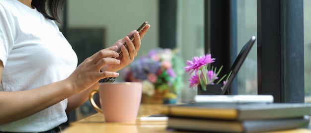 Mains féminines à l'aide de smartphone assis à un espace de travail portable au café