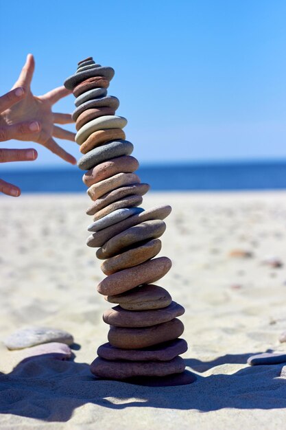 Des mains féminines attrapent un cairn qui tombe sur une plage de sable Des pierres d'équilibre Zen instables