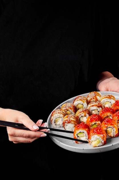 Mains féminines avec des baguettes prenant un rouleau de sushi au saumon et au caviar rouge dans une assiette