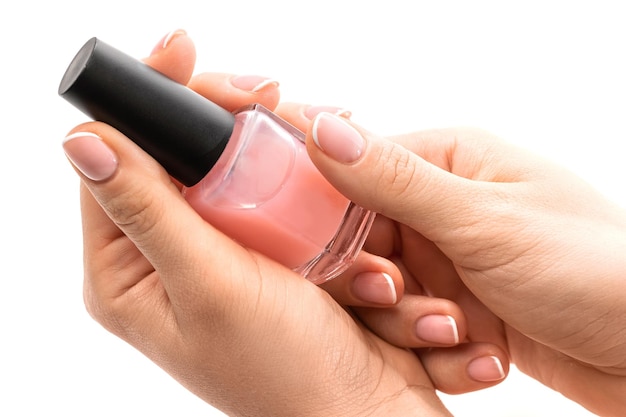 Mains féminines avec une belle manucure française tenant une bouteille de vernis à ongles rose sur fond blanc