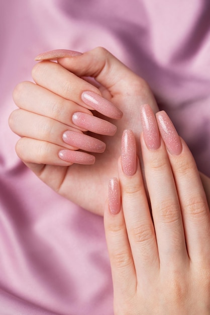 Des mains féminines avec une belle manucure sur de la soie rose