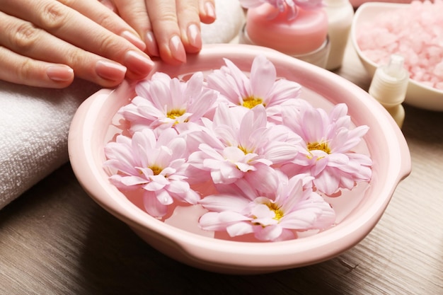 Des mains féminines et un bol d'eau de spa avec des fleurs en gros plan