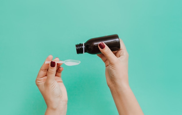 Mains féminines avec une bouteille de sirop de médecine. Femmes versant du sirop contre la toux dans une cuillère