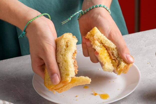 Photo des mains féminines brisant un sandwich avec du miel et du beurre d'arachide de pain de blé pour le petit déjeuner