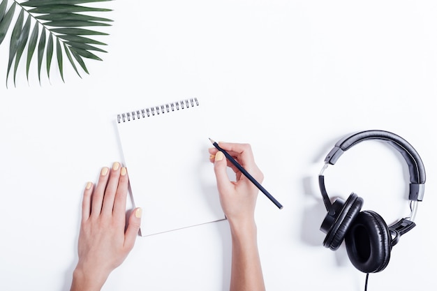 Mains féminines avec un carnet et un crayon, des écouteurs et des plantes sur tableau blanc