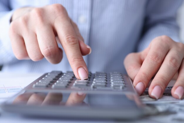 Les mains féminines comptent sur la calculatrice au gros plan de la table