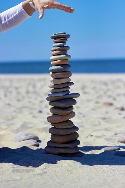 Les mains féminines construisent une pyramide de pierres sur une plage de sable sur fond de mer