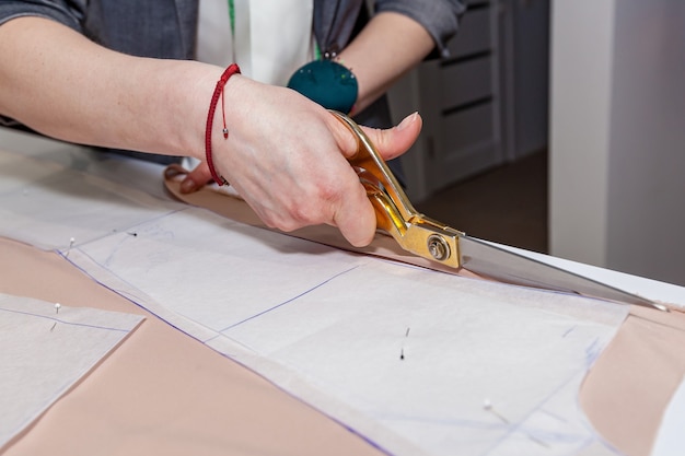 Des mains féminines coupent le tissu avec des ciseaux de tailleurs sur le motif du papier, sur un tableau blanc