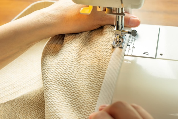 Mains féminines cousant du tissu blanc sur une machine à coudre moderne Vue rapprochée du processus de couture