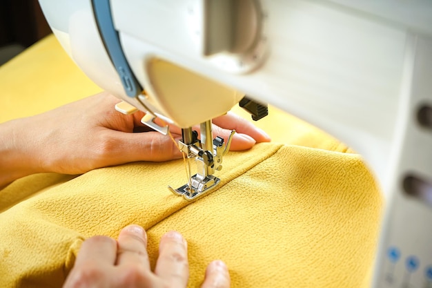 Mains féminines cousant du tissu jaune sur une machine à coudre moderne Vue rapprochée du processus de couture