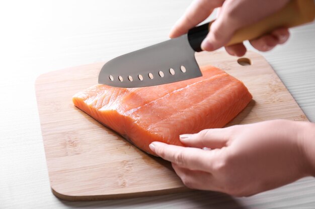 Des mains féminines avec un couteau coupant du filet de saumon frais sur une planche de bois
