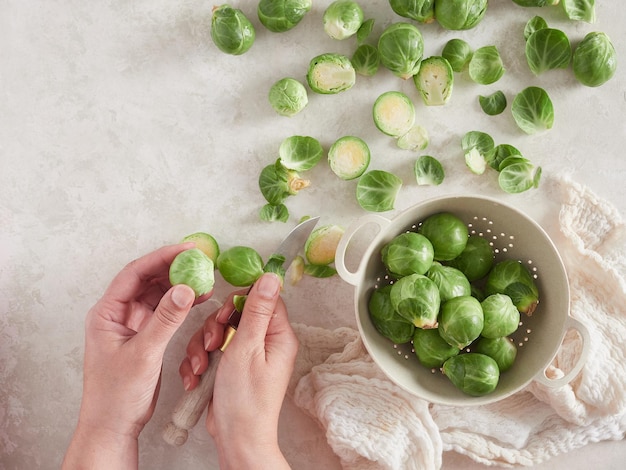 Mains féminines avec couteau épluchant les choux de Bruxelles Préparation des légumes crus pour la cuisson sur le comptoir Vue de dessus