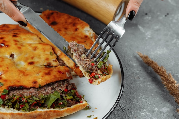 Mains féminines avec un couteau et une fourchette coupées Khachapuri avec de l'agneau et du piment