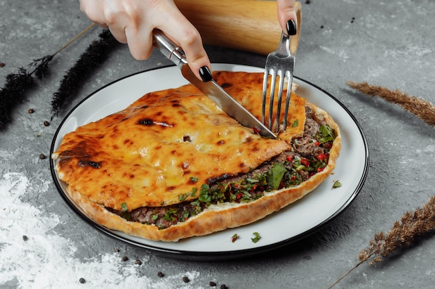 Des mains féminines avec un couteau et une fourchette coupent Khachapuri avec de l'agneau et du piment. Cuisine nationale géorgienne.