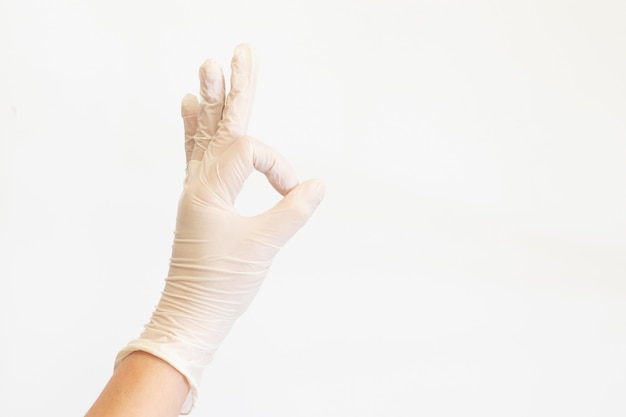 Mains féminines dans des gants médicaux blancs montrant signe ok.