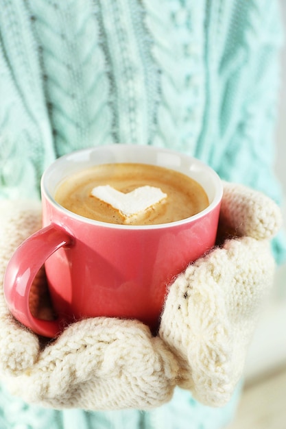 Mains féminines dans des mitaines chaudes tenant une tasse de cappuccino chaud avec guimauve coeur gros plan