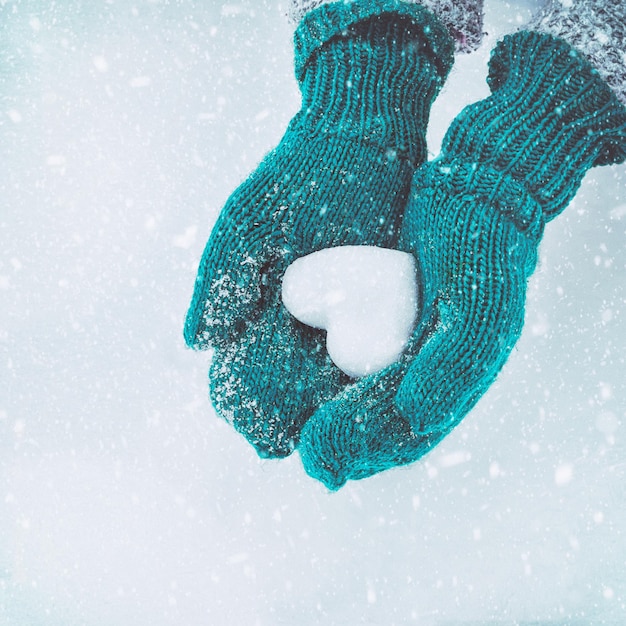 Photo mains féminines dans des mitaines tricotées avec coeur de neige en journée d'hiver. notion d'amour.