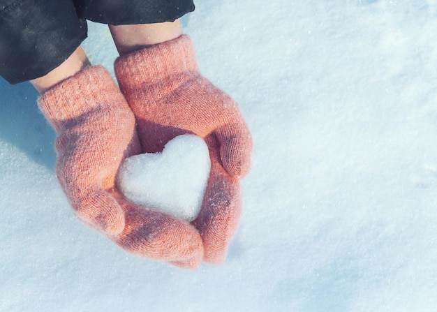 mains féminines dans des mitaines tricotées avec coeur de neige en journée d'hiver. Notion d'amour.