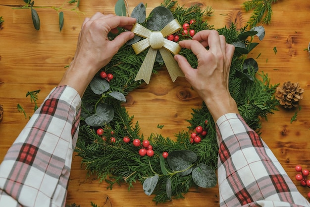 Des mains féminines décorent une couronne de Noël avec un ruban et un arc